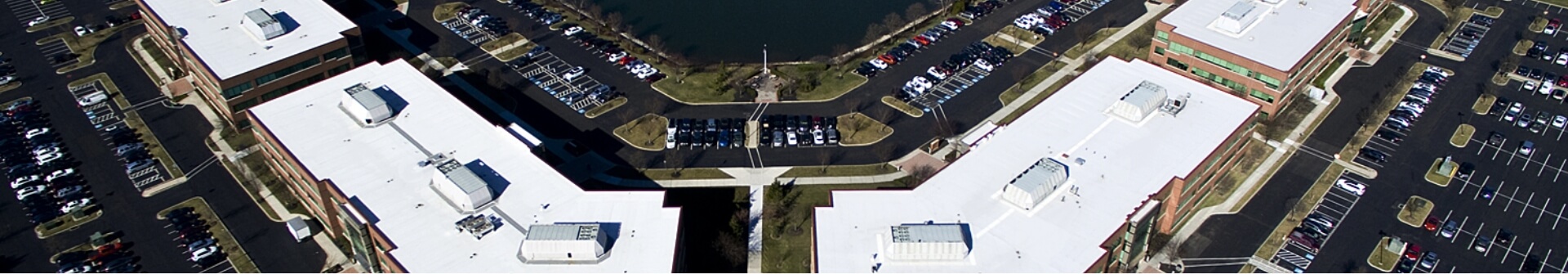 an aerial view of four separate buildings with white roofs surrounded by a parking lot