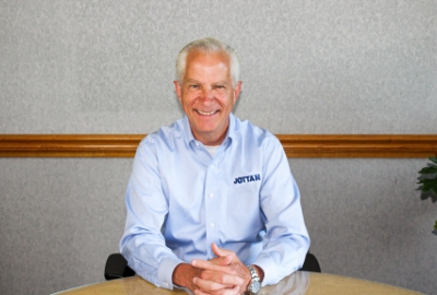 a man wearing a shirt that says Jottan sits at a table with his hands folded