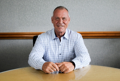 a man in a plaid shirt sits at a table with his hands folded