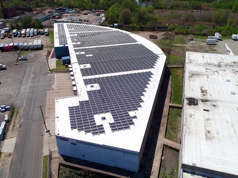 an aerial view of a large building with solar panels on the roof with trucks in the background
