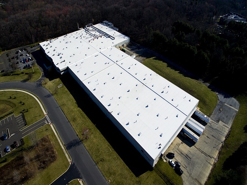 an aerial view of a large building with a white roof surrounded by grass and a small road