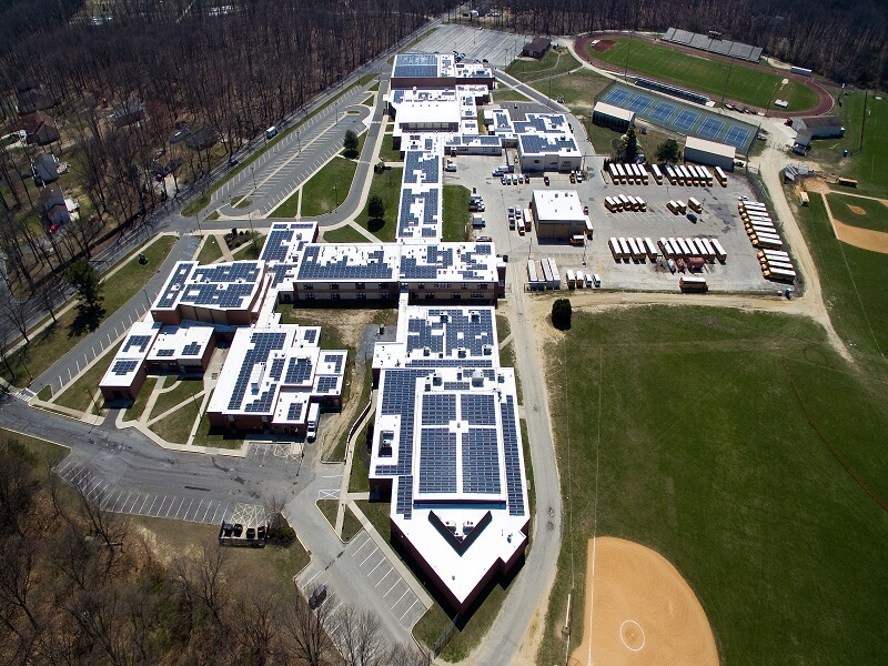 an aerial view of a school with solar panels on the roof with a baseball field in the front right corner