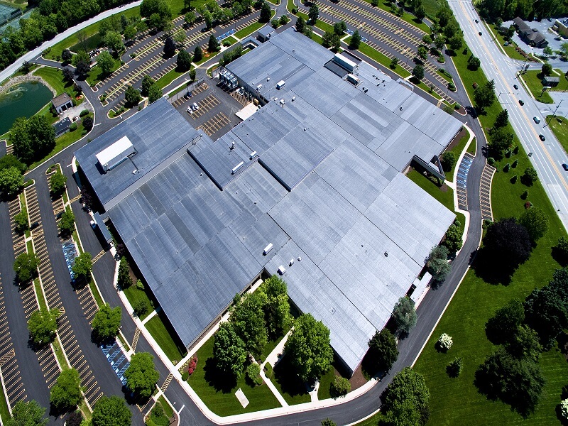 an aerial view of a large building with a black roof with a parking lot in front of it