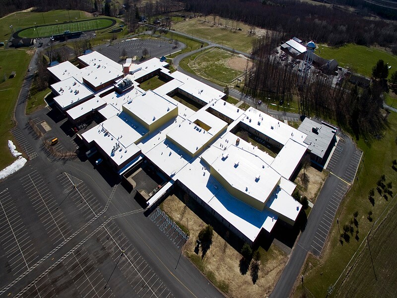 an aerial view of a complex school building with a white roof surrounded by a parking lot