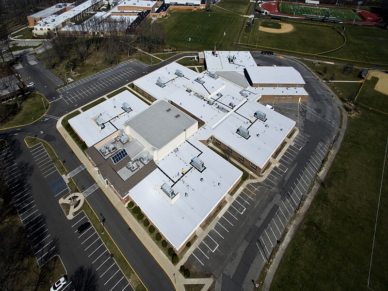 an aerial view of a school with a white roof surrounded by an empty parking lot